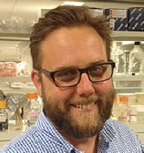 Formal headshot of faculty member Justin Kollman in lab.
