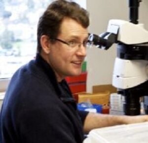 Formal headshot of faculty member Brian Kraemer in lab, seated in front of microscope.