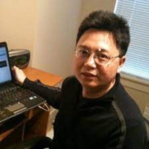 Headshot of faculty member Qingahang (Chris) Liu in office, seated in front of laptop.