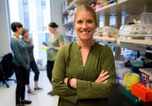 Formal headshot of faculty member Jessica Young in lab with lab members in background.