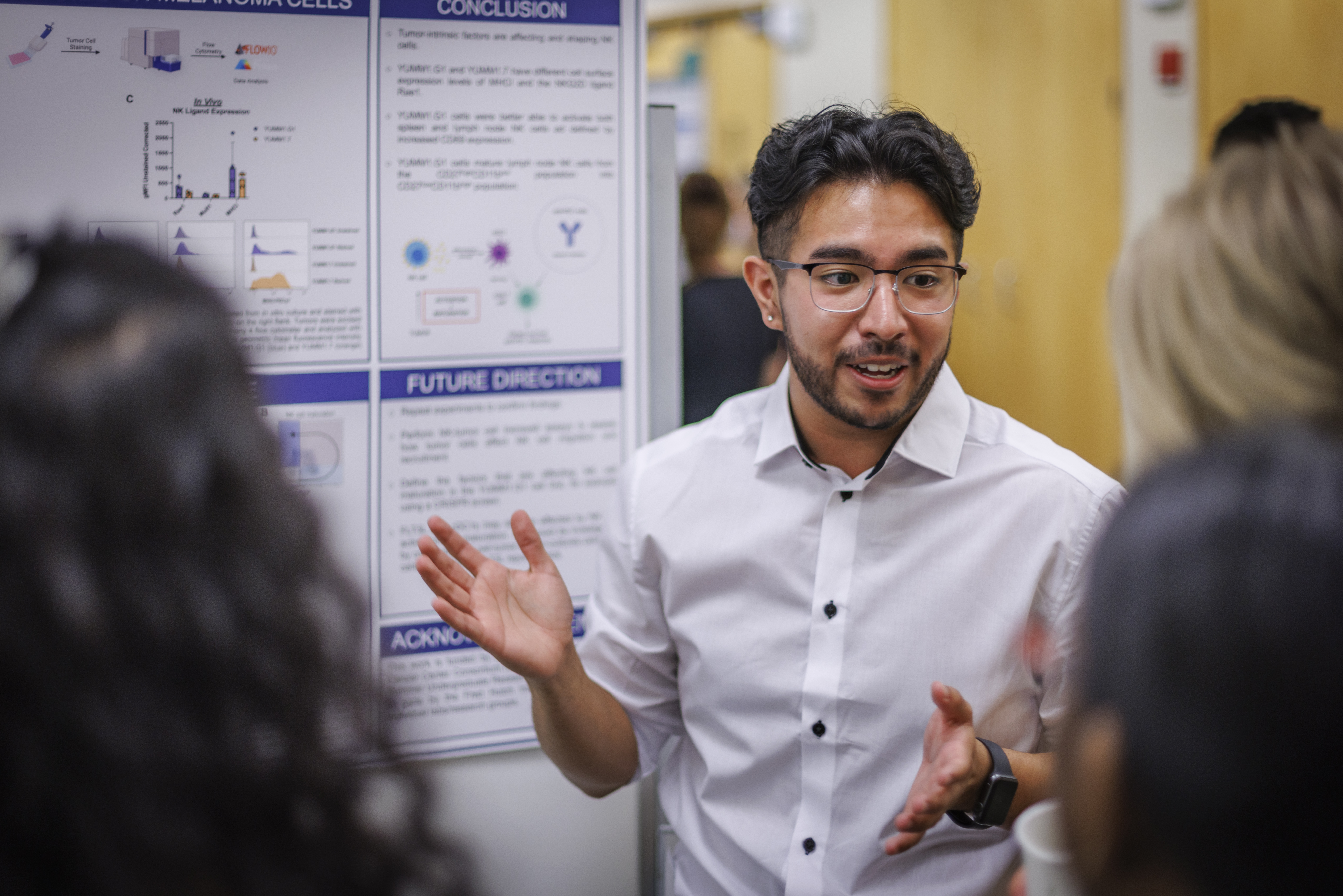MCB student presenting research poster to three individuals standing at his poster.